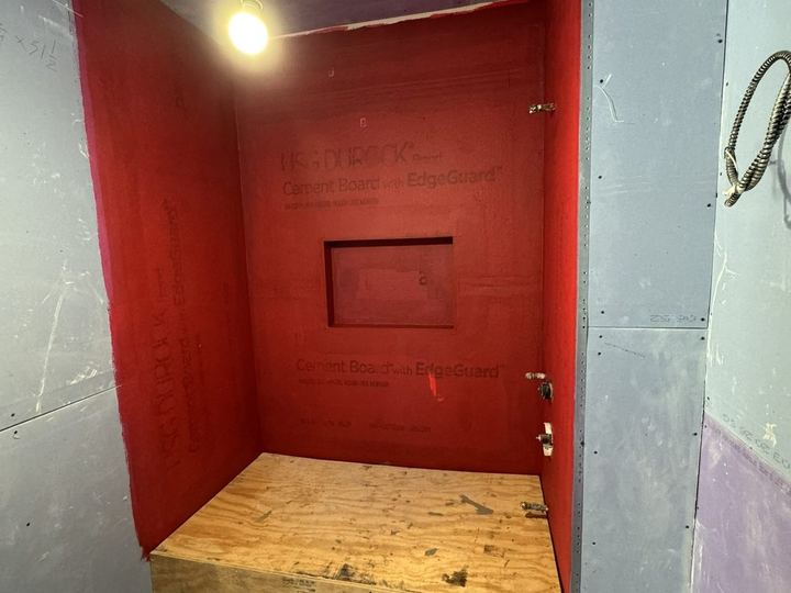 Red cement board on the shower walls, with a niche and a bench framed in - Sani Building Corp