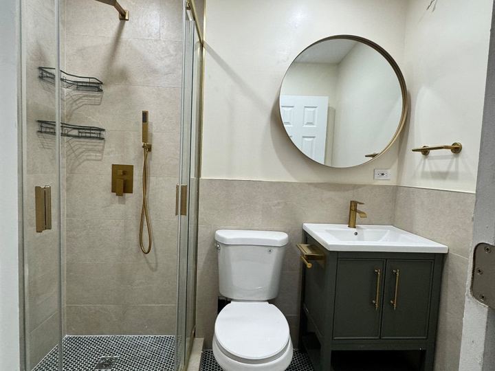 Bathroom with a glass shower, brushed-gold fixtures, a round mirror and a dark green vanity - Sani Building Corp