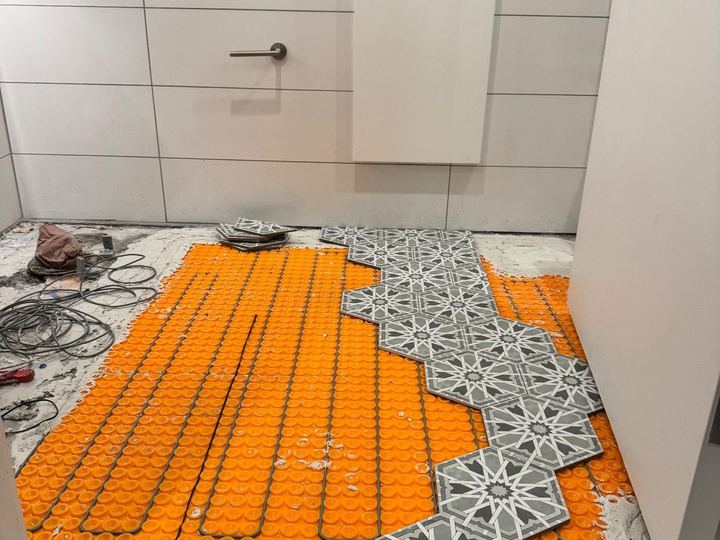 Patterned floor tile going down over an orange underlayment membrane - Sani Building Corp