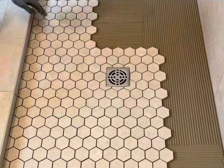 Hexagon mosaic floor tile being set around a shower drain - Sani Building Corp