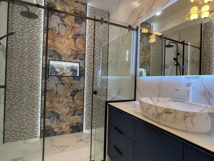 Glass walk-in shower with a floral feature wall, a lit niche and a marble vessel sink - Sani Building Corp