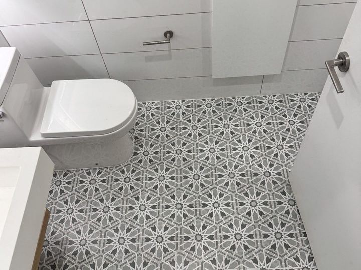 Patterned gray and white floor tile around a wall-hung toilet - Sani Building Corp