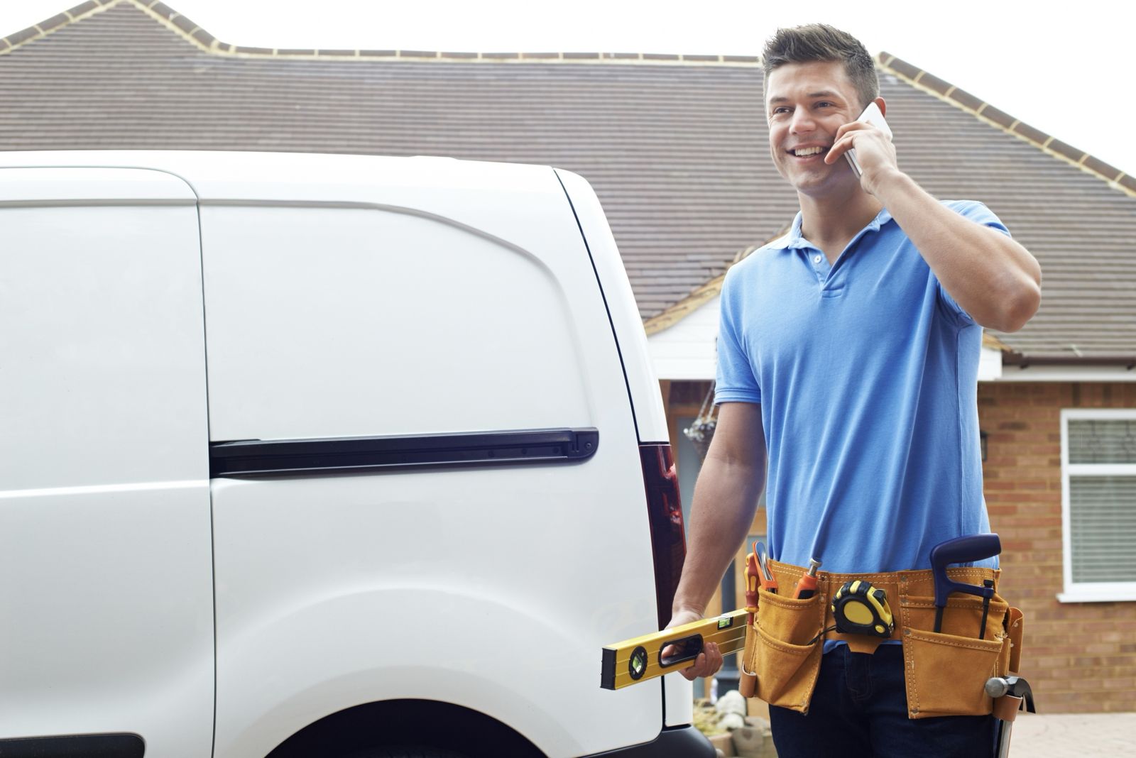 Handyman with a tool belt and level next to a work van, on the phone with a customer in Manhattan